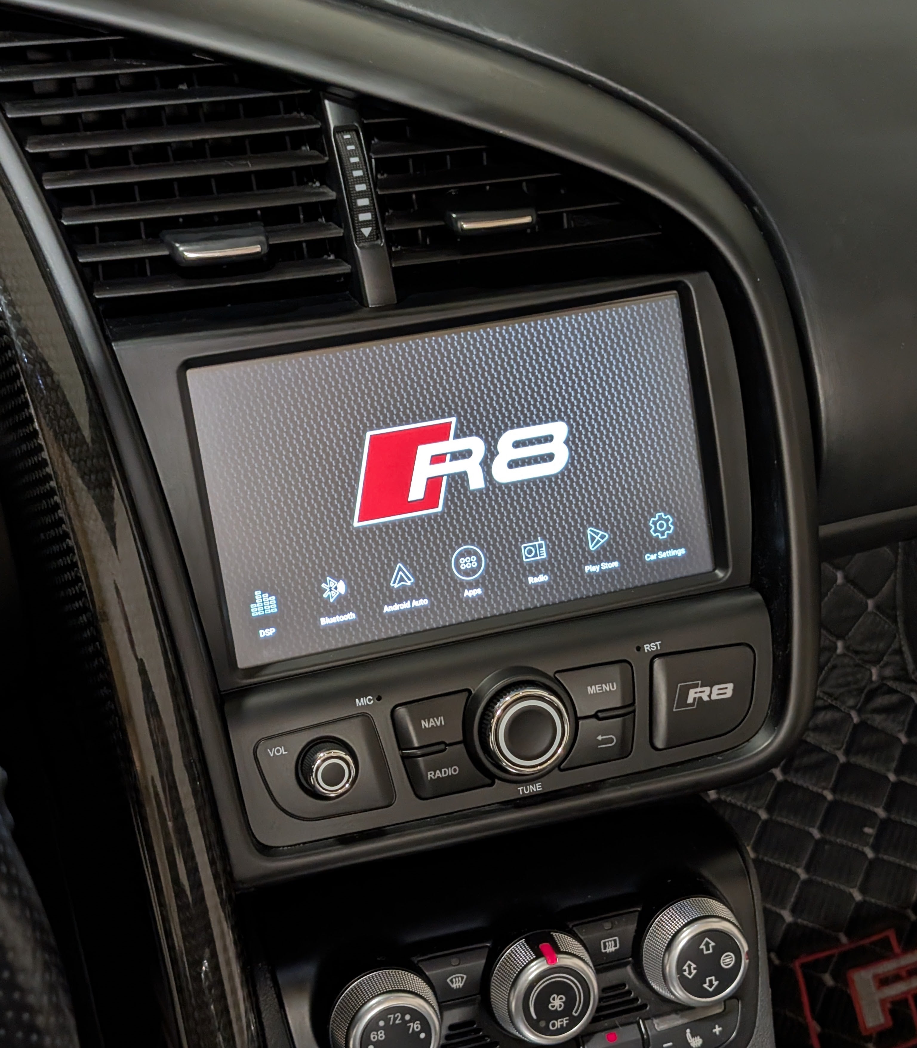 Car dashboard with a digital display showing the Audi R8 logo.